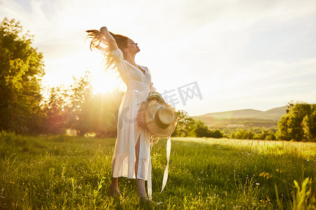 水平照片中，一位身穿浅色长裙的女子穿过森林，夕阳的光芒从背后照亮，头发拉直