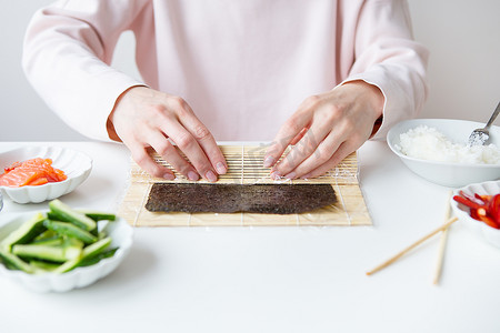 寿司准备过程中，女孩制作不同口味的寿司-新鲜三文鱼、鱼子酱、鳄梨、黄瓜、生姜、米饭。