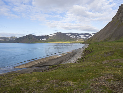 北部夏季景观，沙滩，可欣赏美丽的积雪悬崖和阿尔夫斯费尔山，霍恩斯特兰迪尔的赫洛杜维克湾，西部峡湾，冰岛，绿色草地，蓝天背景