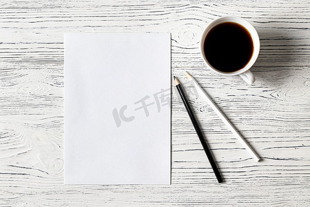 一杯咖啡摄影照片_白纸、铅笔和一杯咖啡放在木桌上。