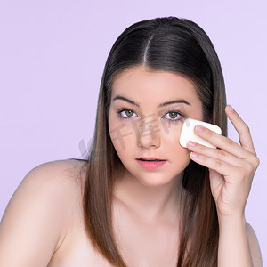 年轻迷人的女孩在脸上涂抹干粉粉底的肖像。