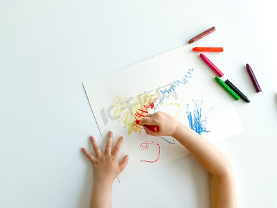 小孩子用蜡笔在白桌上画画。