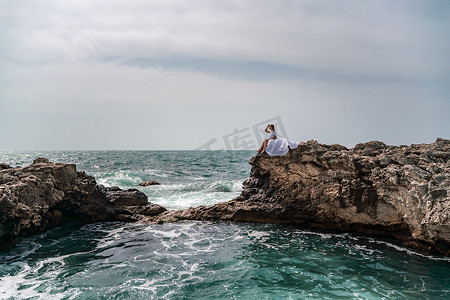 暴风雨中的一个女人坐在海中的一块石头上。