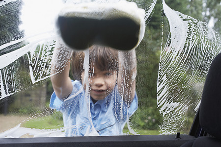洗车玻璃摄影照片_小男孩用海绵从车内看洗车