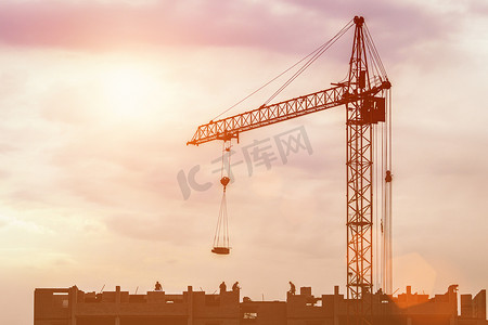 一群建筑工人的剪影和一台起重机在日落天空的背景下建造一座建筑物。