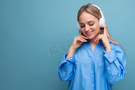 特写迷人的女孩在蓝色孤立的背景下高兴地戴着大耳机听播客