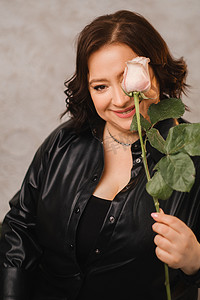皮衣摄影照片_一位穿着黑色皮衣的时尚成年女性站着，里面放着一束粉红玫瑰