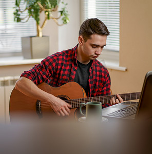 放松的年轻人在家弹吉他，用笔记本电脑，喝茶