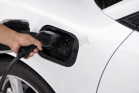 绿色充电汽车摄影照片_特写镜头焦点手插入电动汽车充电器到先进的电动可充电汽车。