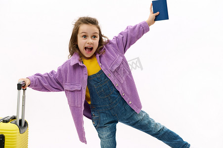 穿着牛仔布工作服、紫色衬衫、黄色手提箱和白色背景登机牌的淘气可爱小女孩