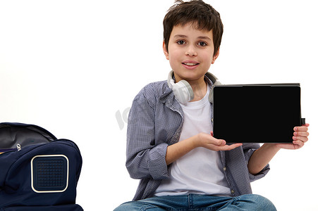 穿着休闲服的迷人少年在镜头前展示一台数字平板电脑，屏幕空空，有可用的广告空间