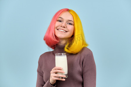 蓝色工作室背景中，美丽微笑的少女模特手里拿着一杯牛奶
