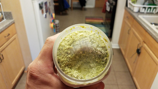 厨房里手持装有冰块的绿色香蒜酱容器