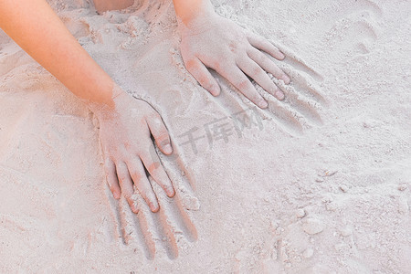 一个小女孩的手躺在温暖的白色沙滩背景上