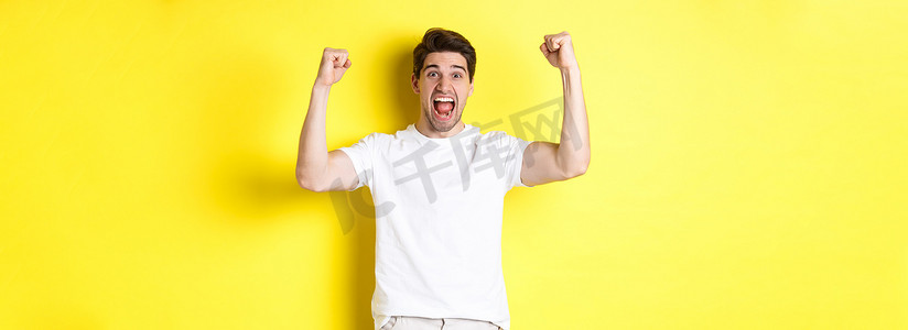 兴奋的男子获胜、举手庆祝、胜利并为团队加油的形象，站在黄色背景上