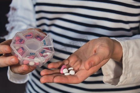 妇女分拣药丸组织者每周拍摄医疗药盒特写镜头，其中装有每日服用的药片剂量，包括白色粉红色药物和胶囊。