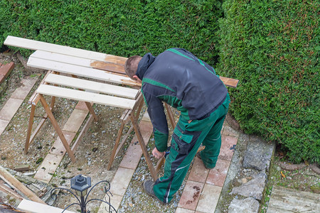 男人在木制花园家具上涂抹保护漆。