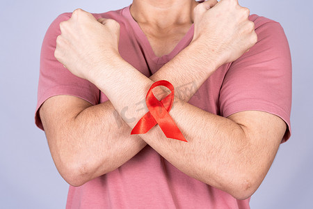 男人手臂上挂着红色艾滋病意识丝带，举起手在灰色背景下与他们作斗争。