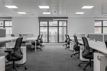 会议中心内空荡荡的灰色调办公室，配有桌椅和大型落地窗。