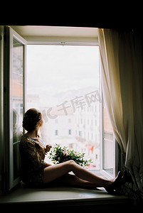 开窗户的人摄影照片_拿着一束鲜花的女人坐在窗台上，看着开着的窗户