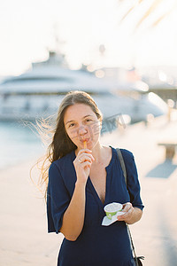 码头上用杯子里的勺子吃冰淇淋的年轻女人