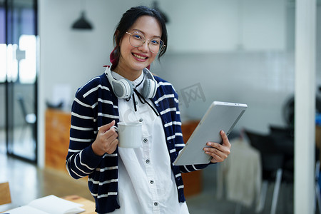 一位亚洲少女的肖像，她使用平板电脑、戴着耳机、使用笔记本在图书馆的木桌上通过视频会议在线学习