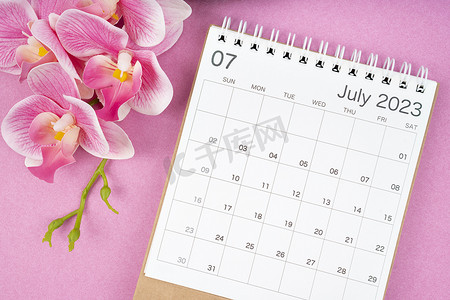 2023 年 7 月日历桌和粉红色背景上的粉红色兰花。