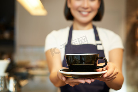 裁剪镜头，女咖啡师手拿着一杯咖啡，给你饮料，在咖啡馆服务，穿着制服