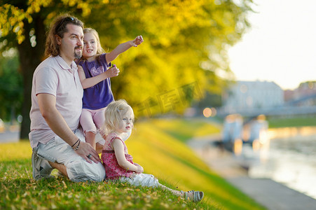年轻的父亲和他的女儿们坐在河边