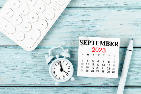 英语活动背景摄影照片_2023年9月月历年和带有蓝色木质背景计算器的闹钟。