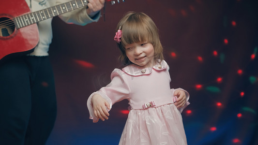 穿着复古连衣裙的小女孩在舞台上跳舞，她的父亲弹着原声吉他