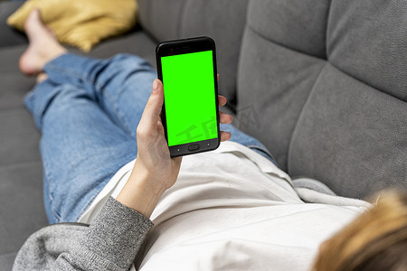 女孩躺在沙发上，拿着一部绿屏智能手机