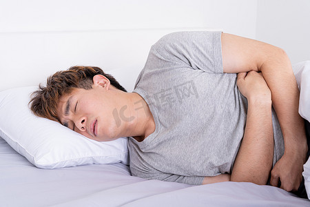 腹疼摄影照片_年轻人躺在床上，肚子疼。