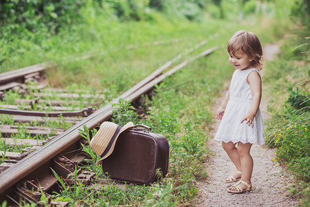 带着手提箱的迷人婴儿沿着铁路行走
