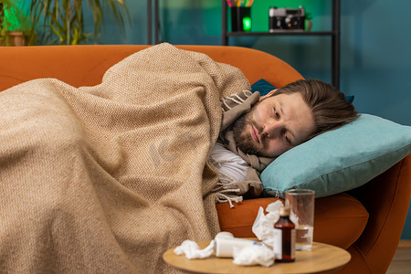 躺在家里沙发上的患感冒或过敏的患病年轻人打喷嚏，将鼻涕擦到餐巾纸上