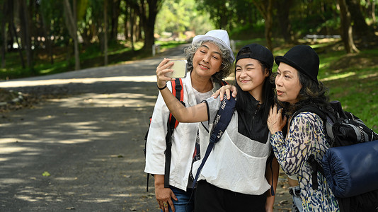 顽皮的亚洲女孩在公园散步时使用智能手机，与可爱的老妇人自拍