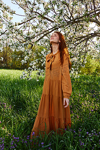 一位快乐、谦虚的女人穿着橙色连衣裙站在一棵开花的树旁，享受大自然和阳光明媚的夏日