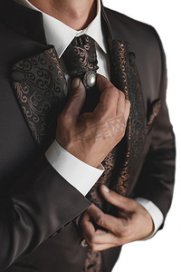珍珠鼠摄影照片_一个身穿白衬衫和棕色豪华西装的男人用双手特写调整带珍珠的领带
