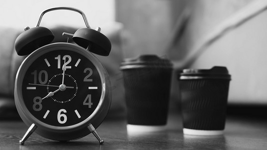 早晨闹钟摄影照片_两杯卡布奇诺和一个带闹钟的复古时钟，公寓里的芳香早晨咖啡，杯子里的美式咖啡，箭头在上午 8 点，特写。黑白图片。