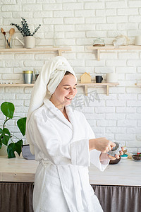快乐的年轻女人在自家厨房的脸上涂抹面部磨砂膏