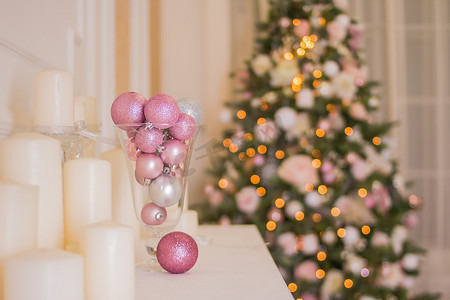 圣诞树内饰，室内粉红色装饰的圣诞壁炉，圣诞节的幻想客厅。粉红色和银色装饰品，透明花瓶中的圣诞球，壁炉上的白色蜡烛和窗户旁边有灯的圣诞树。