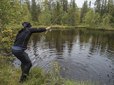 钓鱼者摄影照片_瑞典拉普兰 Kungsleden 徒步小道上的男渔民钓鱼者在小湖中捕鳟鱼