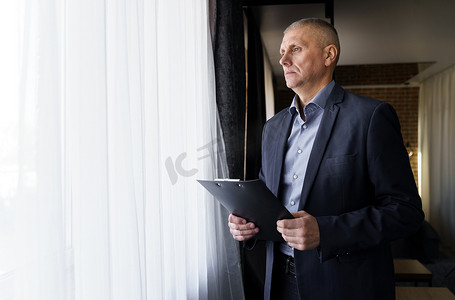 一位商人站着，手里拿着文件，望向窗外的肖像