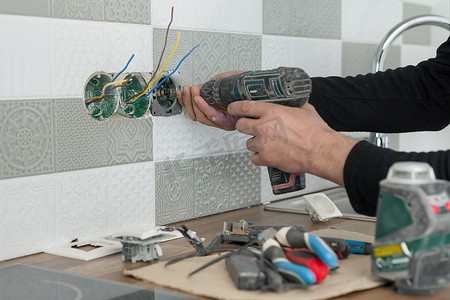 电工在墙上用瓷砖手工安装插座的特写