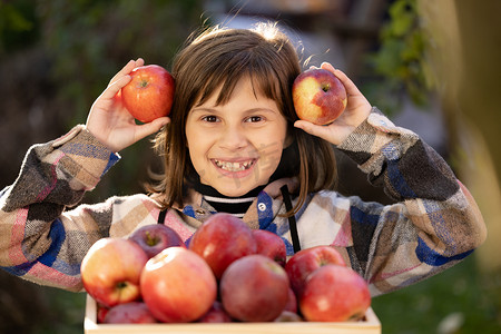美丽微笑的幼儿女孩拿着苹果，脸蛋漂亮，看着相机。