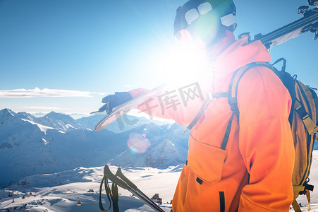 阳光明媚的冬日，一名滑雪者站在山顶上，肩上扛着滑雪板的照片、阳光、户外休闲、滑雪、生活方式、下坡运动概念