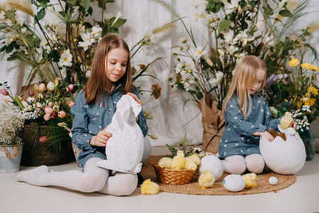 两个女孩在一个美丽的复活节拍照区，里面有鲜花、鸡蛋、鸡和复活节兔子。