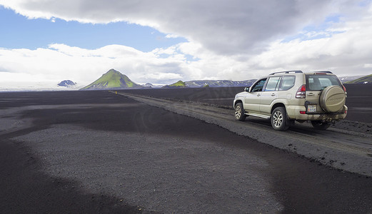 冰岛南部，Fjallabak 自然保护区，2018 年 7 月 7 日：越野车丰田陆地巡洋舰在土山路 F210 上行驶，穿过黑色熔岩沙漠，绿色 Maelifell 山和 myrdalsjokull 冰川，蓝天白云