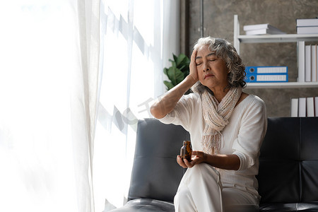 沮丧的亚洲高级女性坐在沙发上，望向窗外。