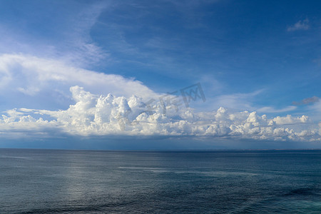 平静的大海和蓝天从船边看，地平线上有弓波尾迹和积雨云。
